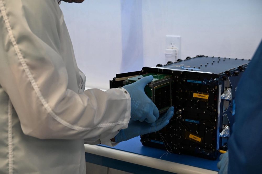 A technician in cleanroom gear handling the satellite before launch